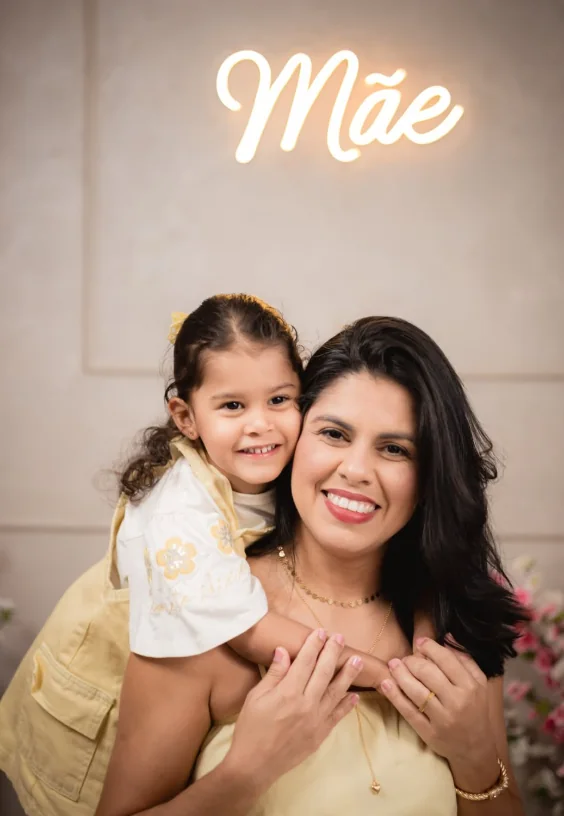 Layse abraçada à filha, com um letreiro luminoso escrito Mãe ao fundo